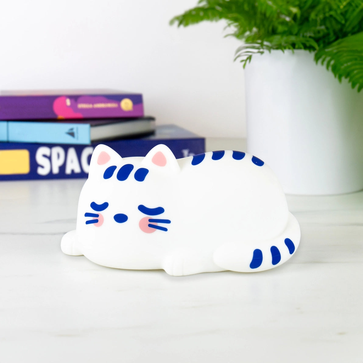 Side view of Catnap Lamp on a desk next to books and a plant – perfect for kids’ rooms or cosy spaces.