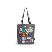 Person wearing grey Beatles tote bag with colourful printed patch designs and black-and-white straps, next to a yellow submarine model.