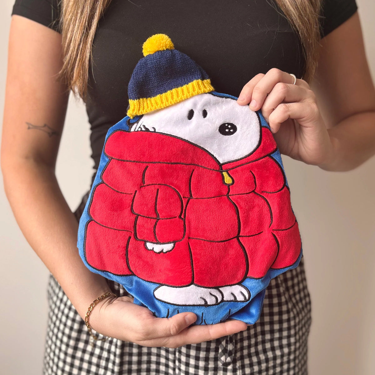 	Woman holding Peanuts Snoopy Puffa Hot Water Bottle with red puffa coat design.
