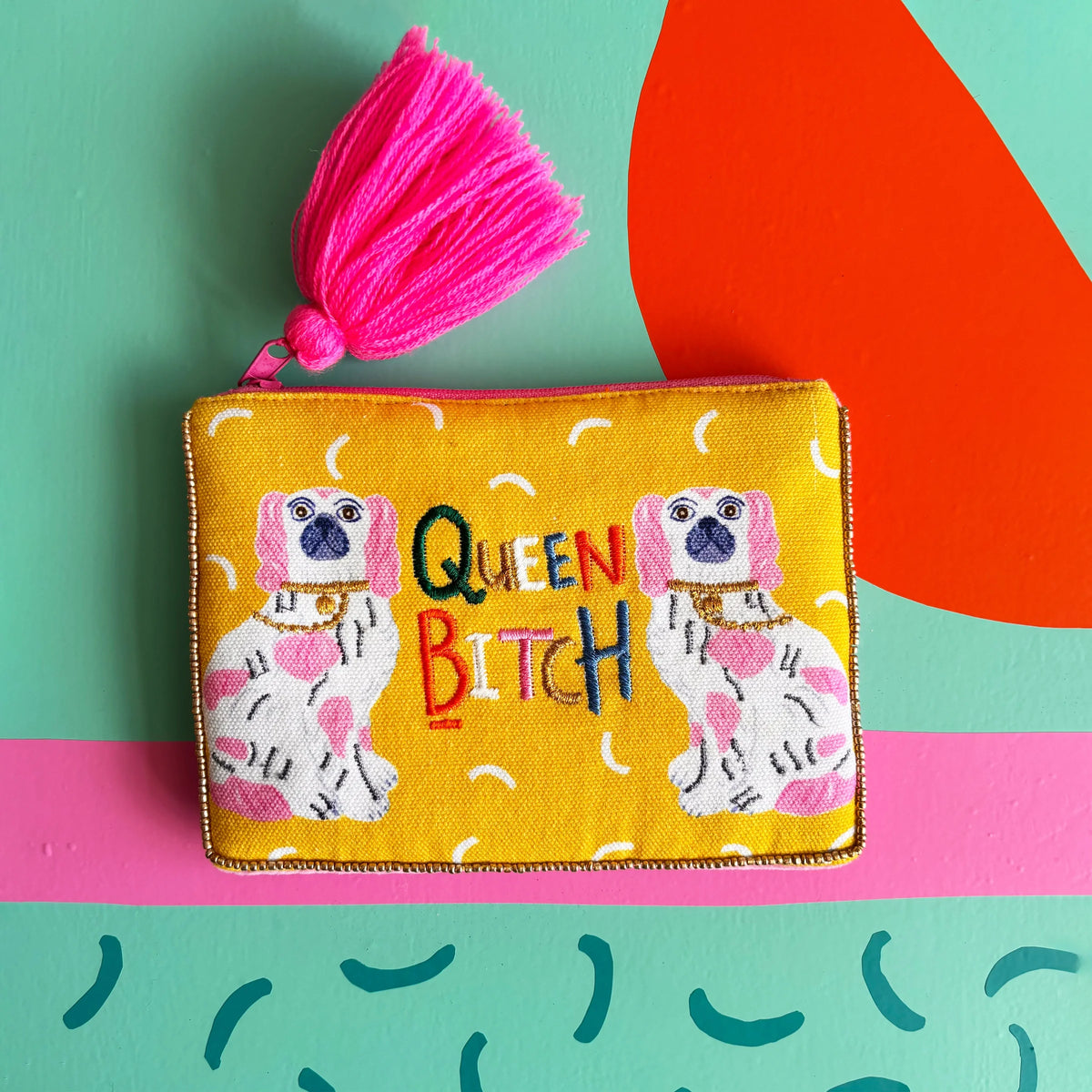 Flat lay of yellow pouch featuring embroidered slogan and dogs.
