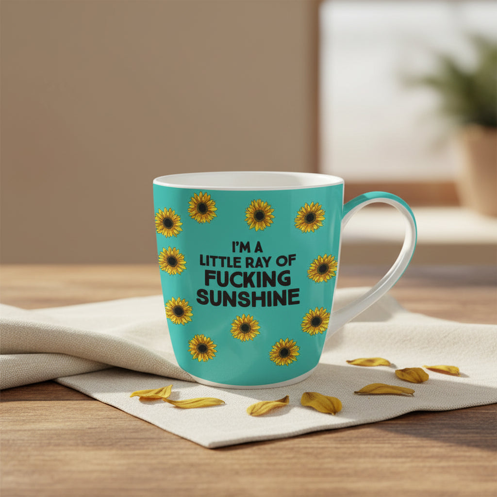 A turquoise ceramic mug with a white interior and handle, decorated with yellow sunflowers and the text 'I'M A LITTLE RAY OF FUCKING SUNSHINE' in bold black letters.