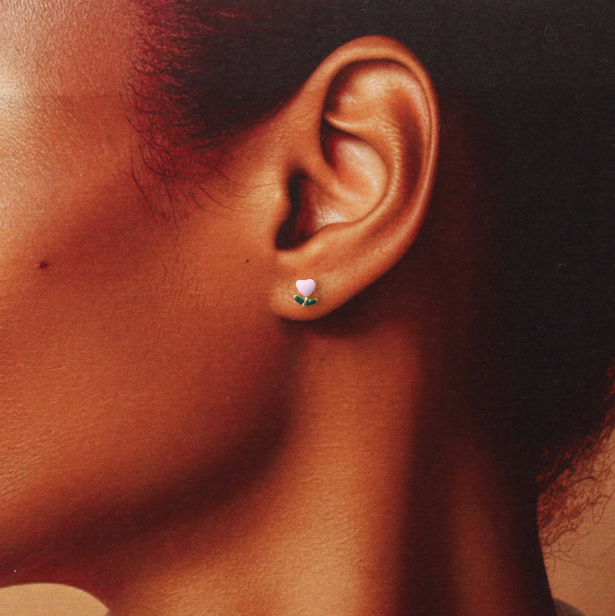 Woman wearing pink enamel flower stud earring in lifestyle close-up