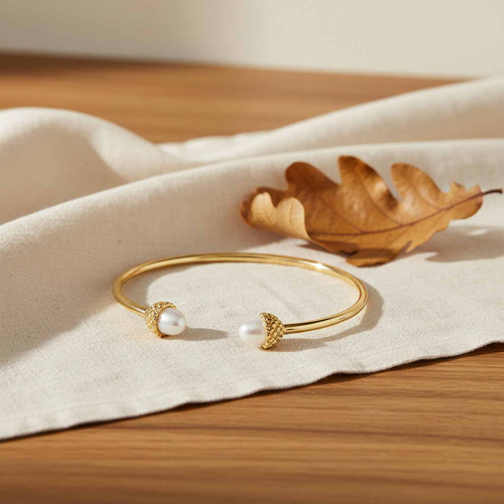 Bill Skinner Acorn and Oak Bangle, open gold cuff with pearl acorn ends, on white