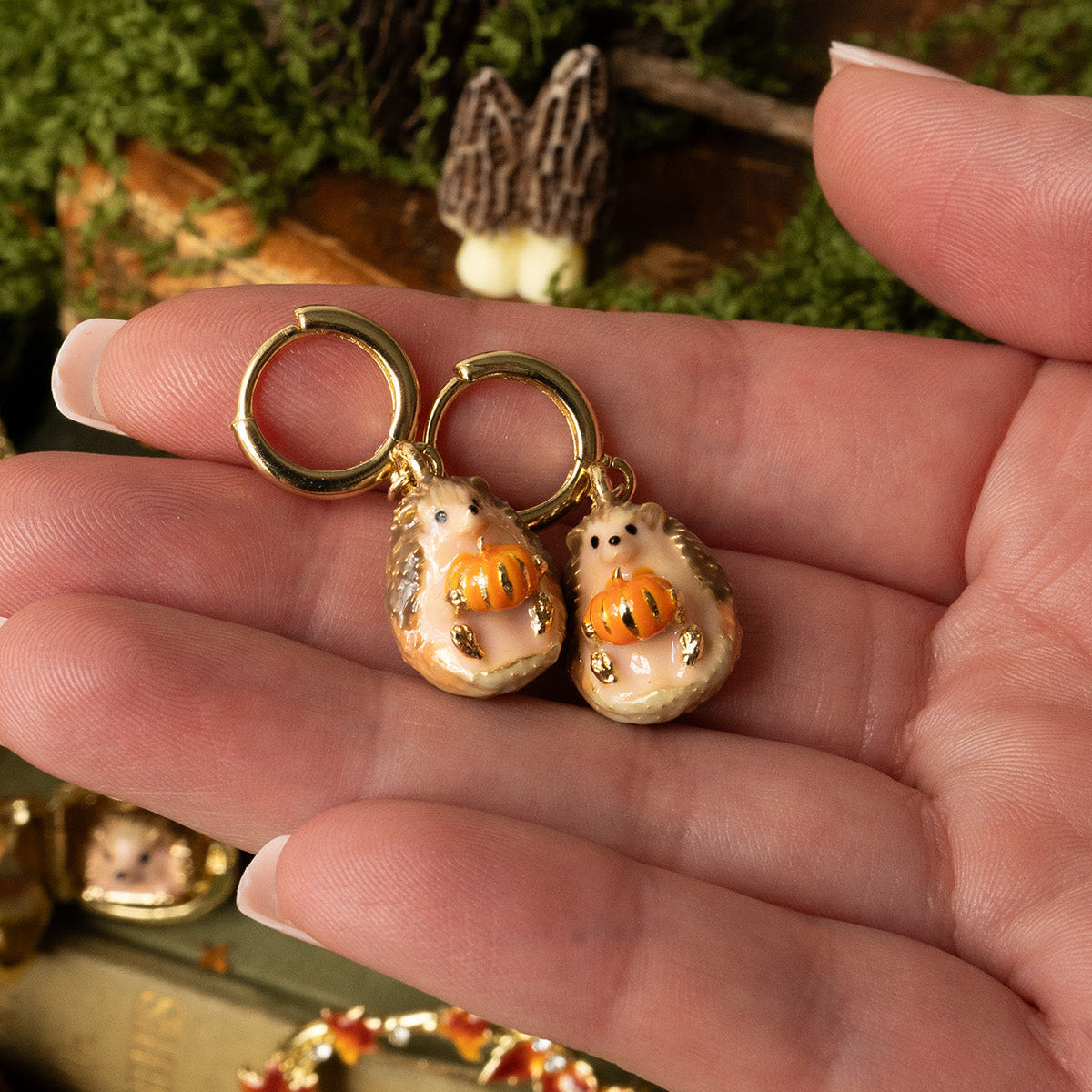Pair of Hedgehog and Pumpkin Huggie Earrings held in an open hand