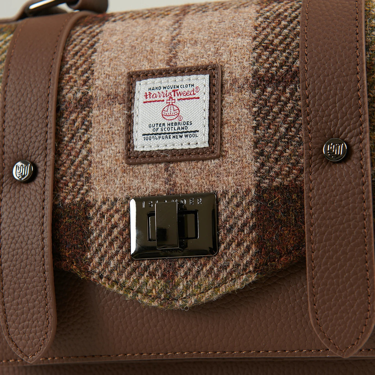 Close-up of chestnut tartan Harris Tweed fabric with leather straps and metal clasp.