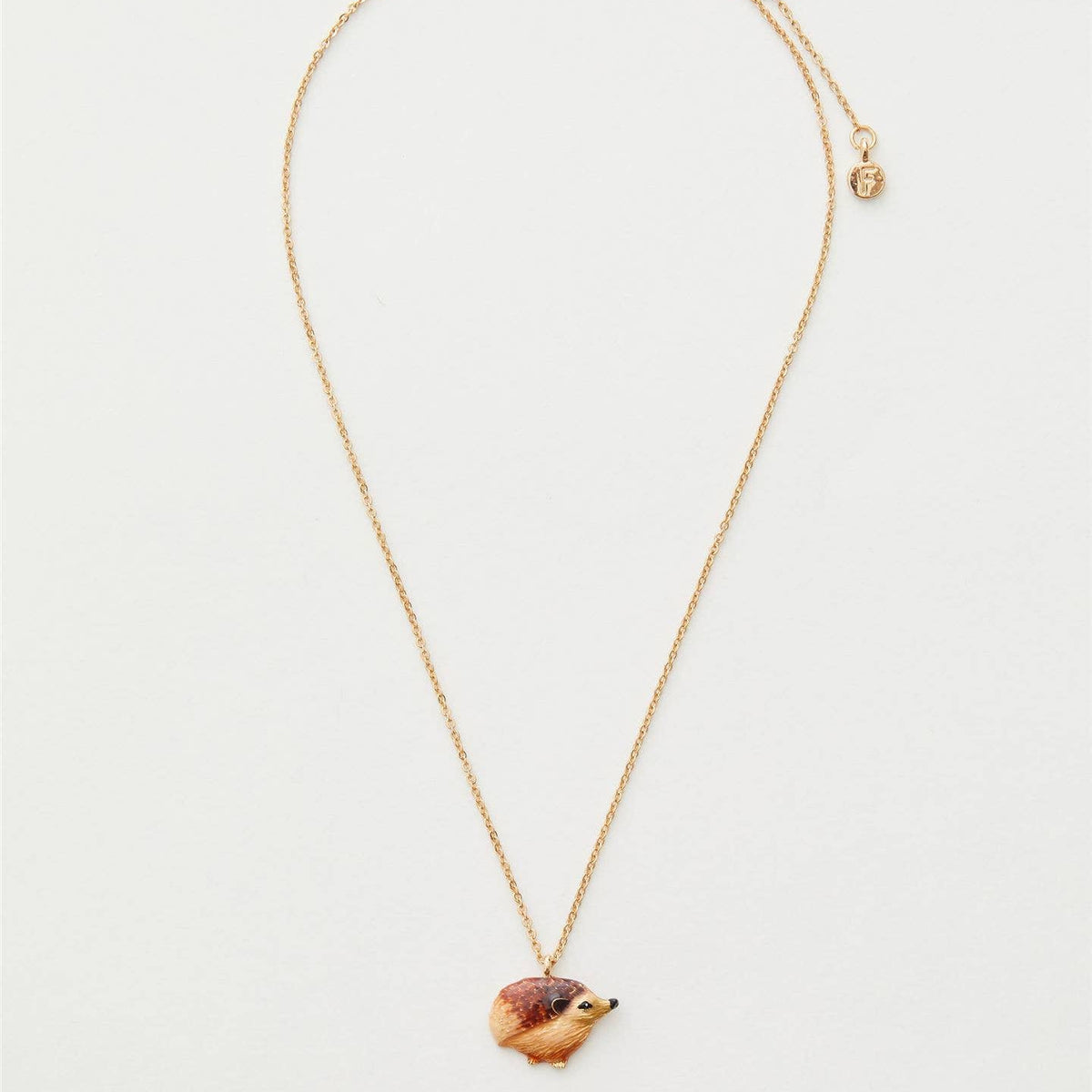 Enamel hedgehog necklace showing full gold chain length on cream background