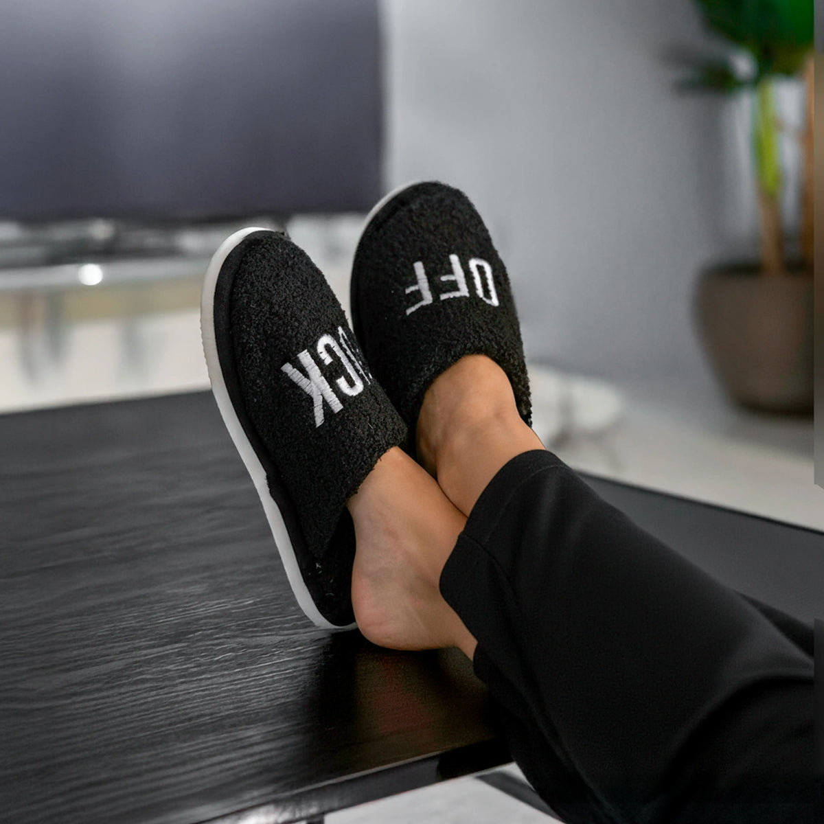 Feet in black slippers resting on a dark wooden floor