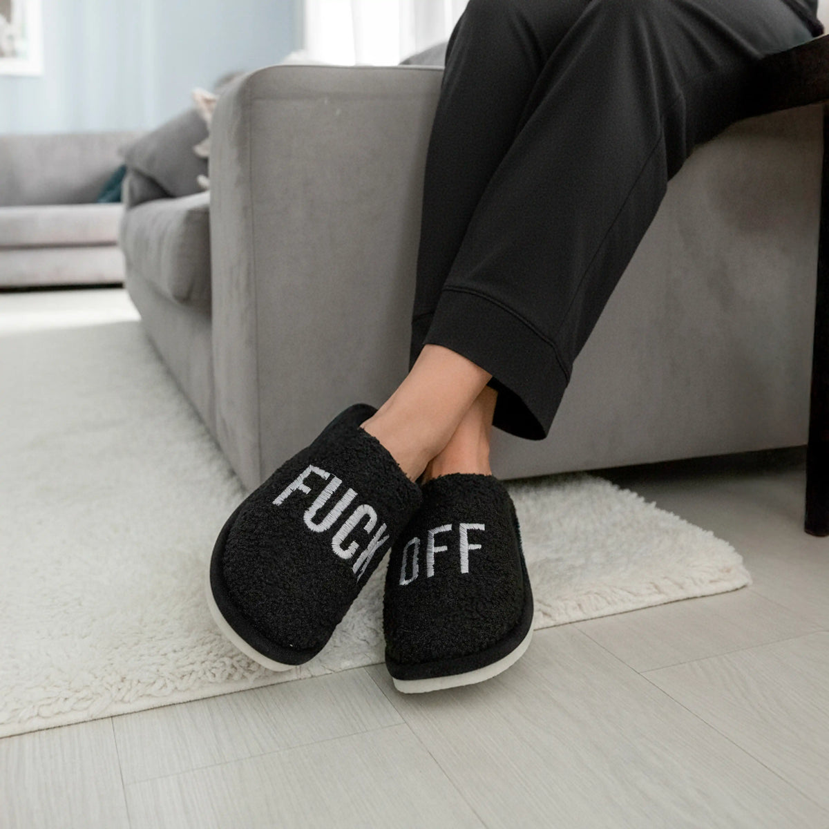 Black slippers on a cream rug beside a light grey sofa