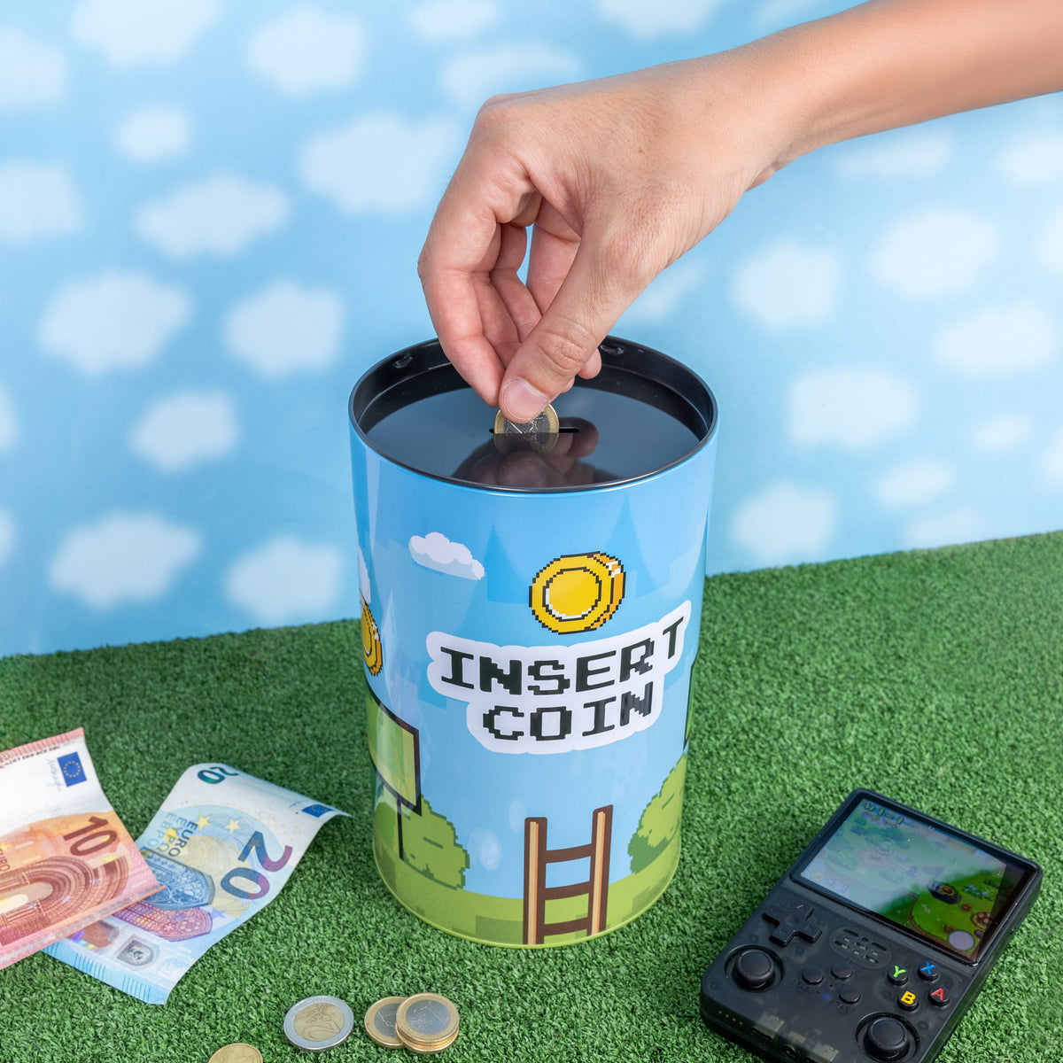 Hand dropping a coin into the Insert Coin tin on green grass