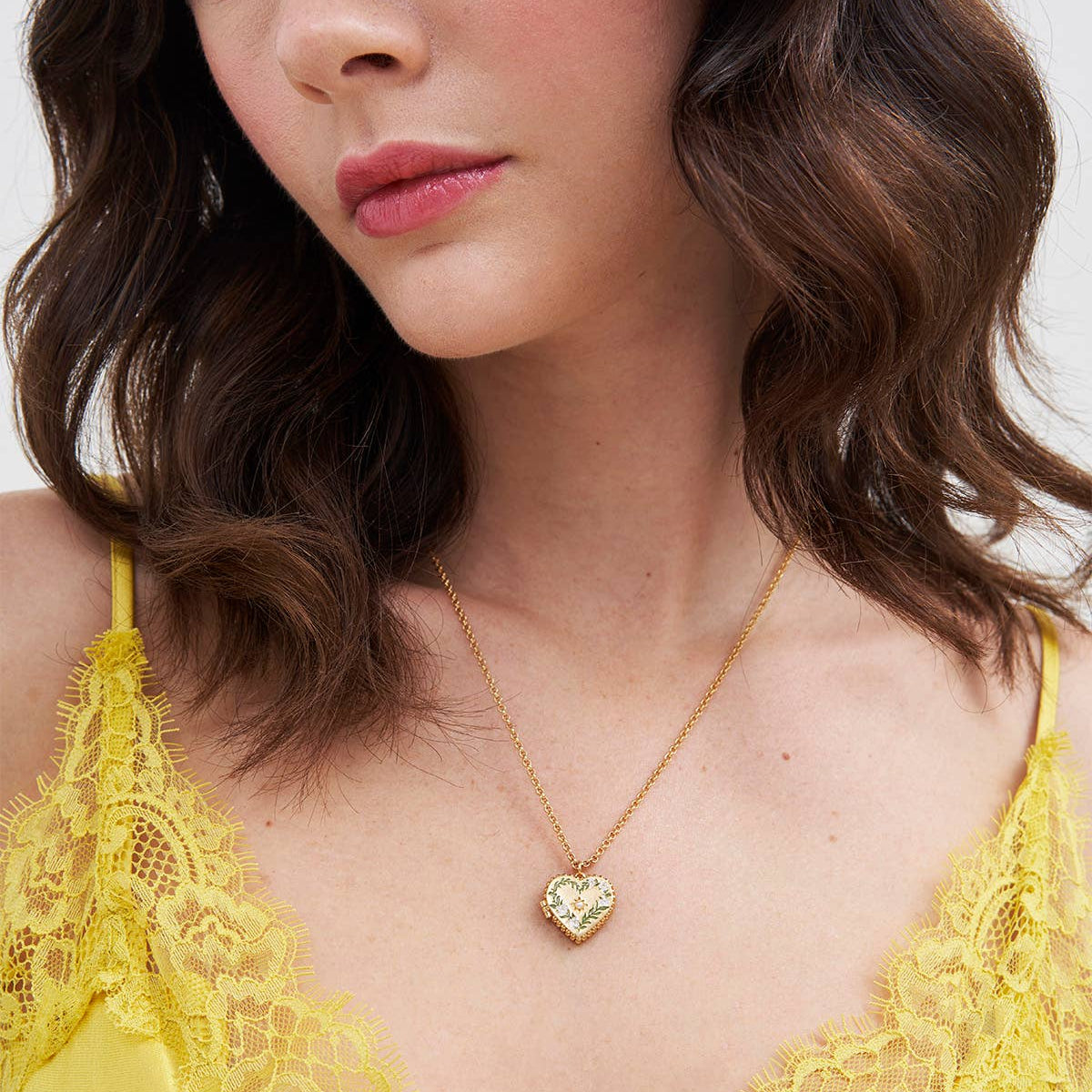 Model wearing Jasmine Heart Locket Necklace in gold with enamel lily detail.