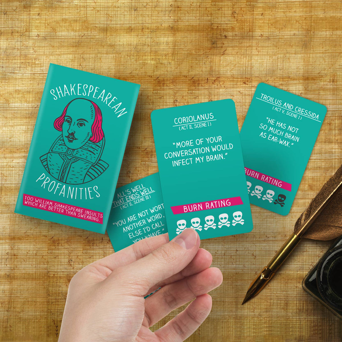 Shakespearean Profanities cards held in hand over parchment and quill