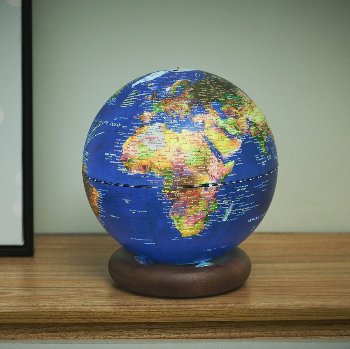 Dark blue globe light lit on a desk beside a picture frame and phone