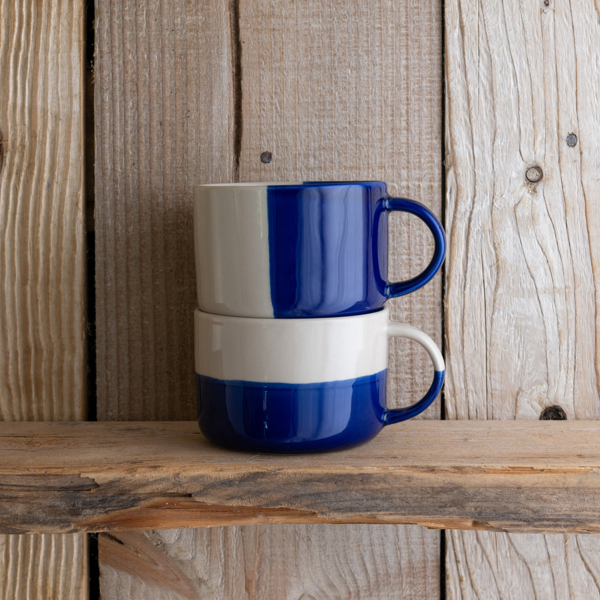 Indigo blue Rue mugs stacked on a weathered wooden shelf