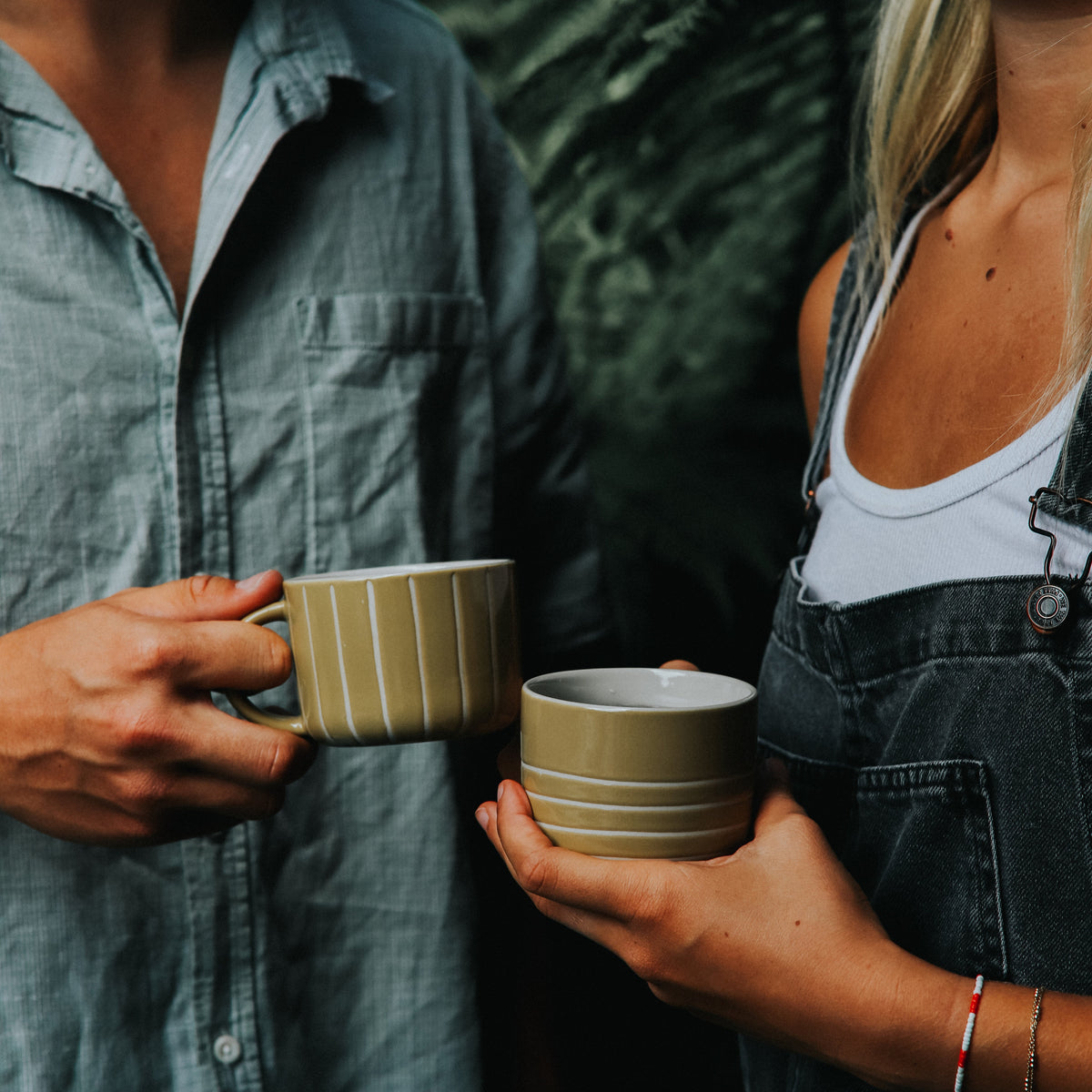 Two people holding mustard yellow Vervain mugs outdoors
