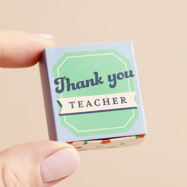Hand holding closed blue matchbox with green label design on cream background