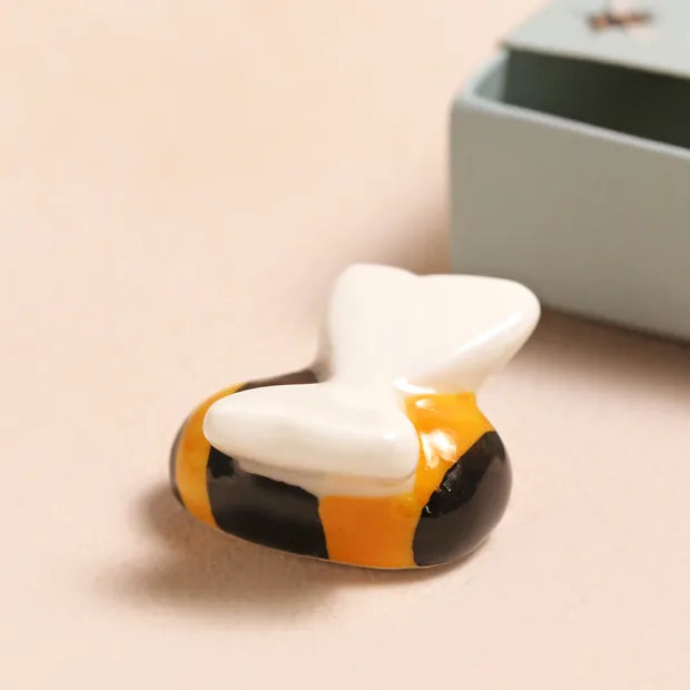 Ceramic bee token with yellow and black stripes and white wings on cream background