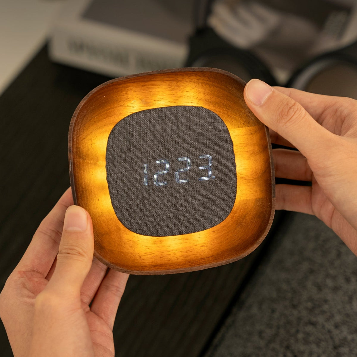 Hands holding lit square walnut Lumos clock close-up