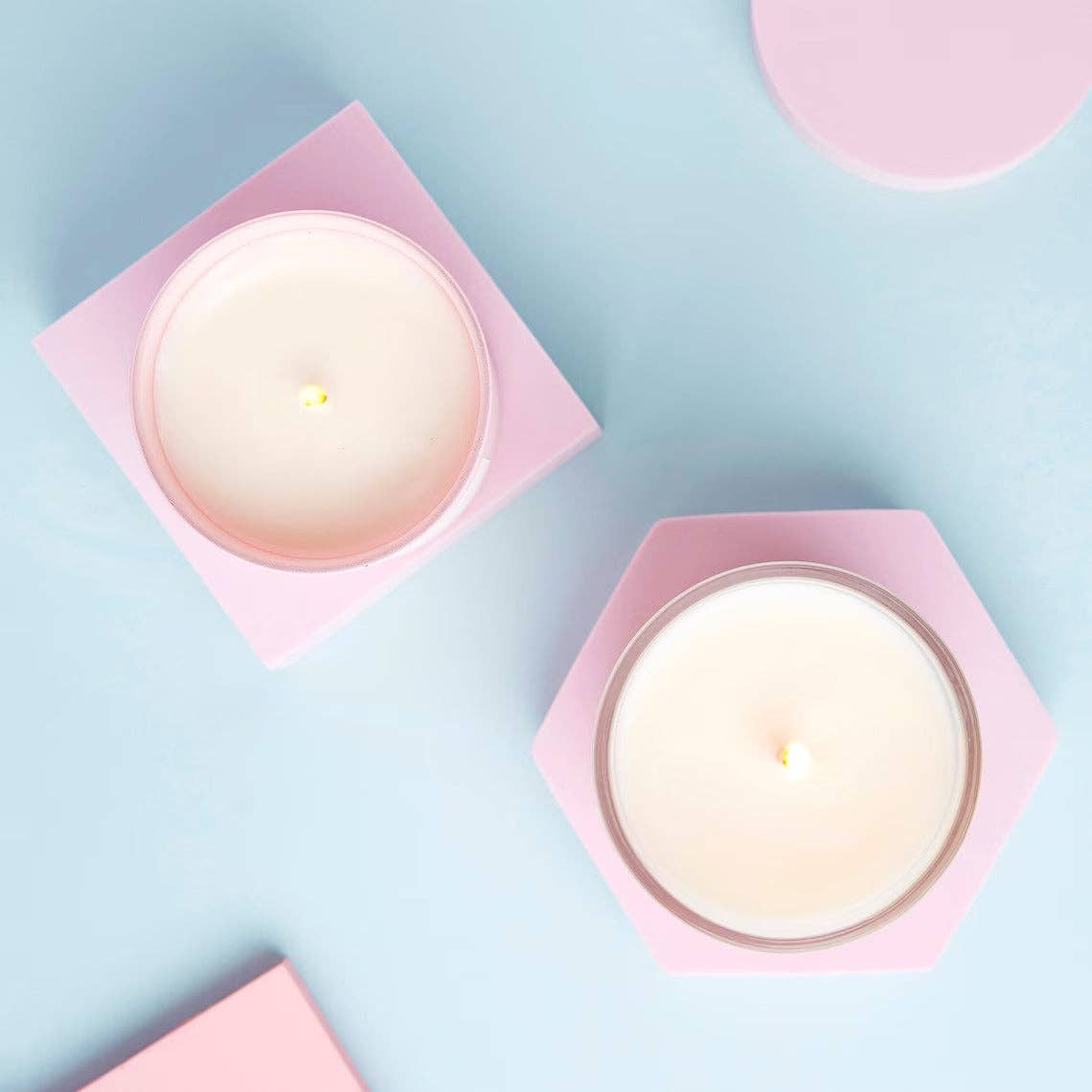 Two lit soy candles viewed from above on pink trays and blue background