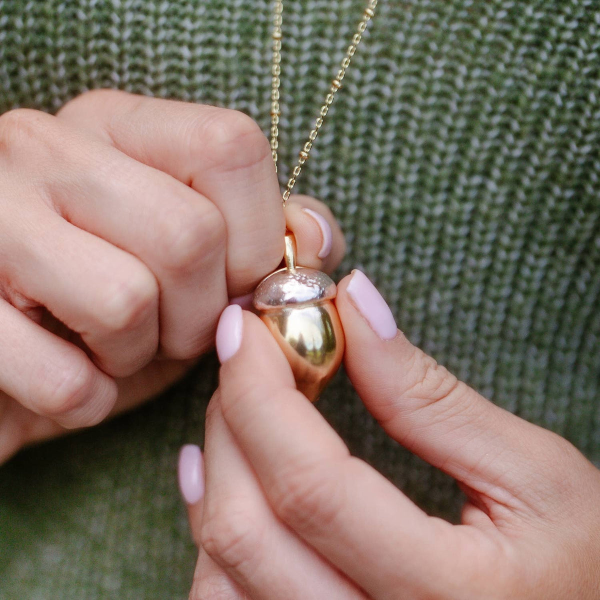 Hands holding closed Squirrel Acorn Locket showing shiny gold and silver two-tone finish.