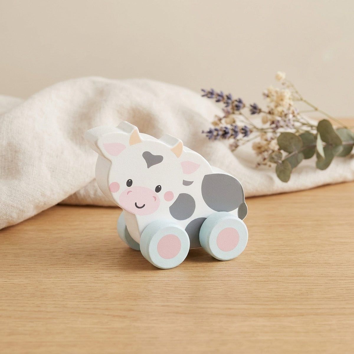Wooden cow push toy on a warm oak table with cream linen and dried flowers