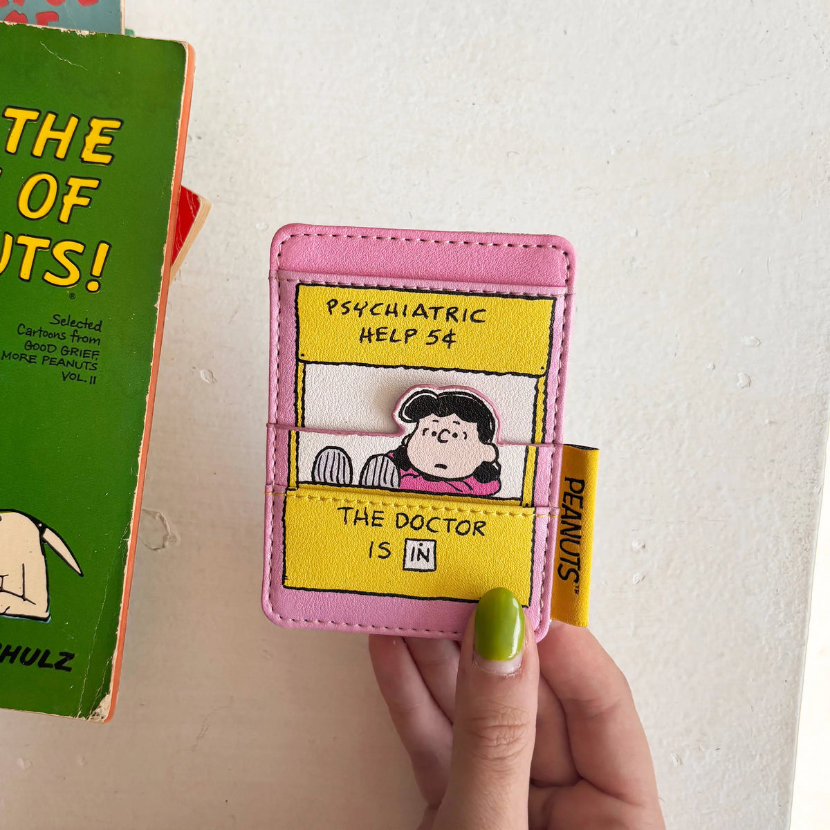 Hand holding Peanuts Lucy Cardholder showing Lucy’s “The Doctor Is In” design.