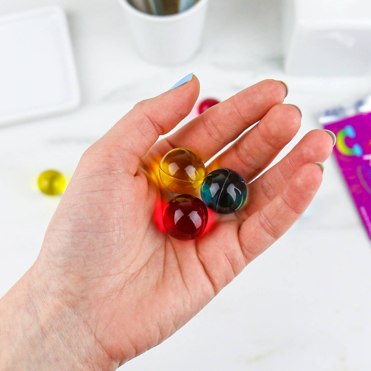 Hand holding three colourful rainbow bath pearls showing glossy texture.